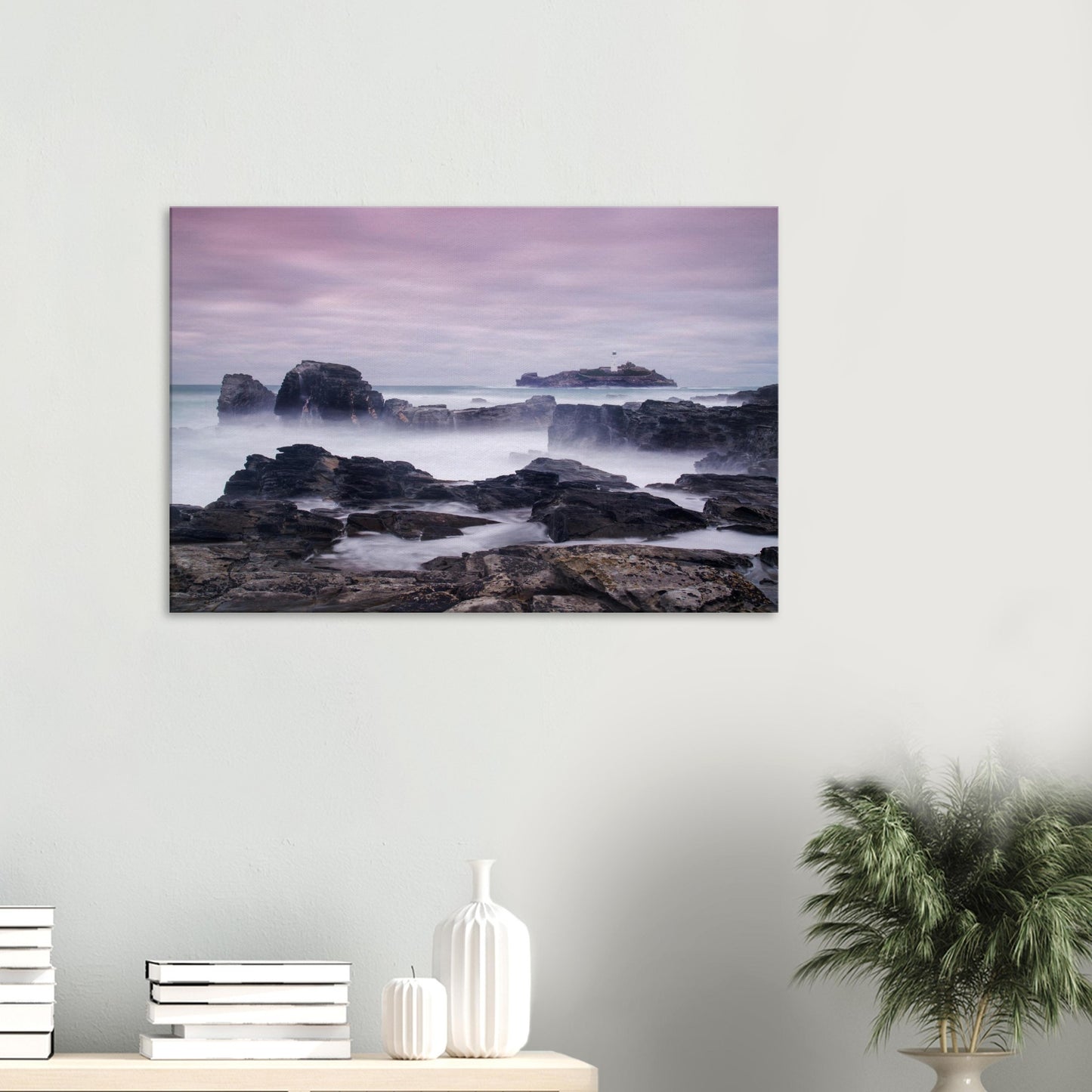 Canvas print of Godrevy Lighthouse in Cornwall, with long-exposure waves misting over jagged black rocks under a pastel sky.