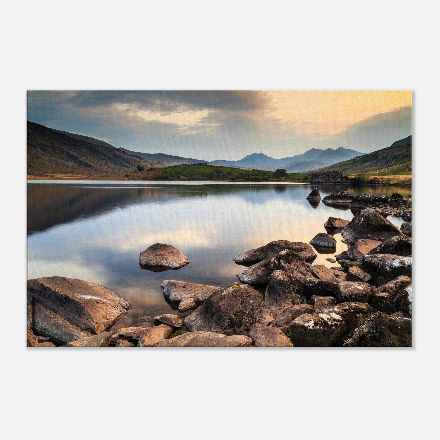 Peaceful Snowdonia lake scene with rocks breaking water surface and distant mountain silhouettes