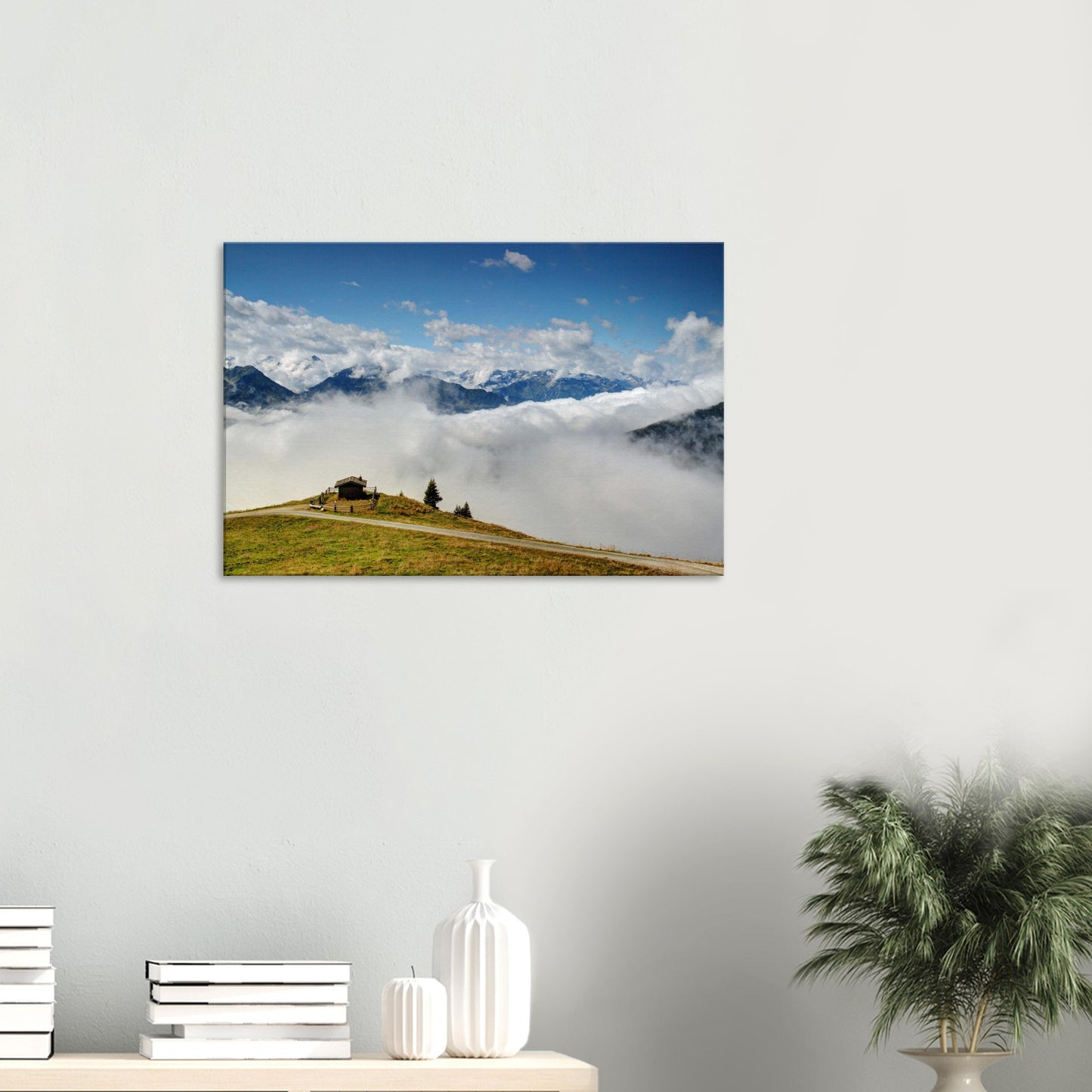 Breathtaking Austrian Alps canvas print showing a solitary hut on a grassy summit with cloud-filled valleys and towering peaks under a blue sky.