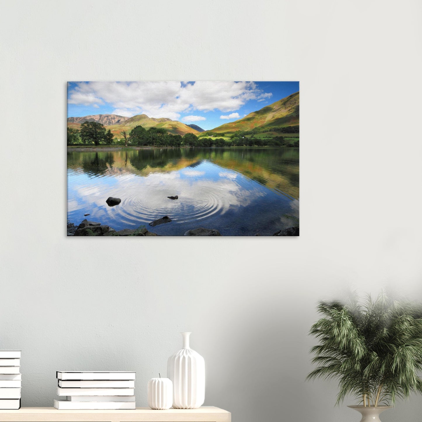 Canvas print of Buttermere Lake capturing the moment a stone disturbs the calm water, reflecting green fells and a cloud-filled sky.