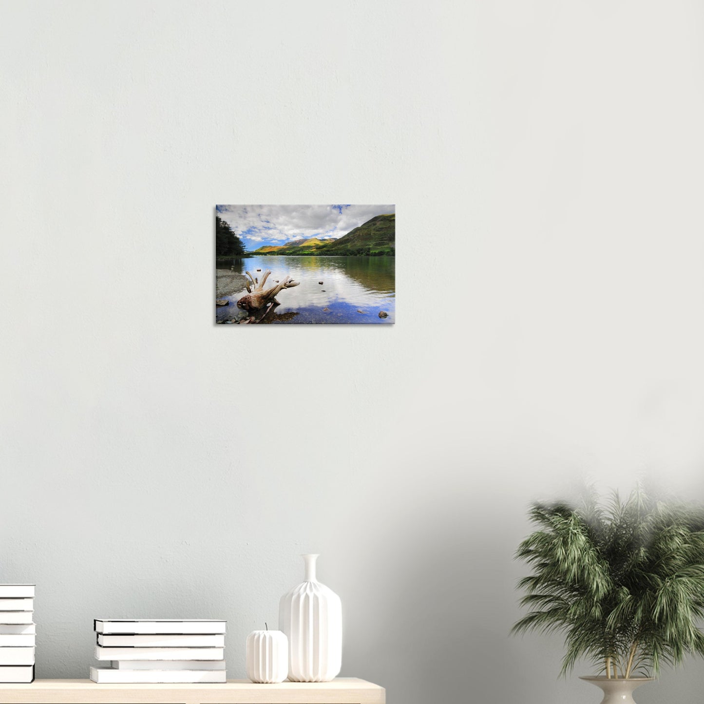Buttermere Lake canvas featuring calm reflective waters, a piece of driftwood on the shore, and bright green fells under a scattered cloud sky.