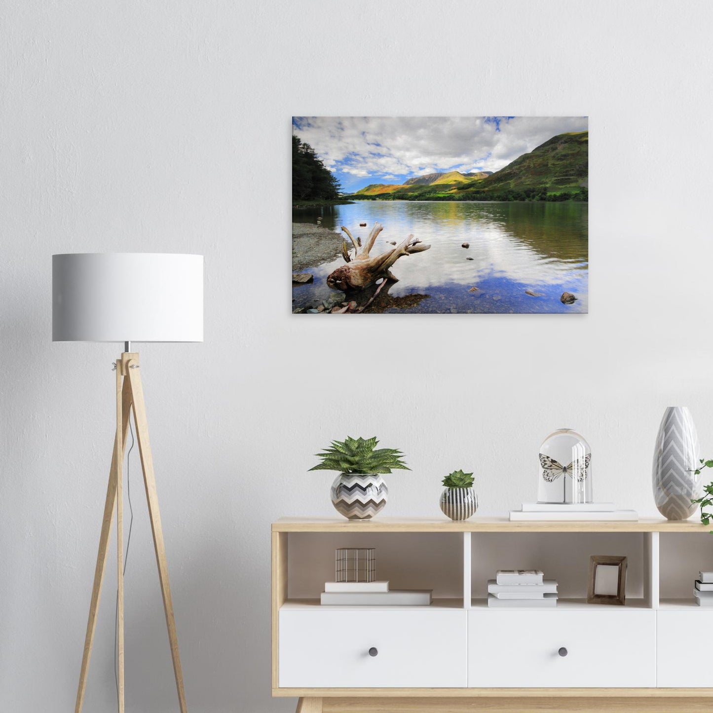 Scenic canvas of Buttermere Lake in the Lake District showing calm waters reflecting clouds and fells, with driftwood resting on the shore.