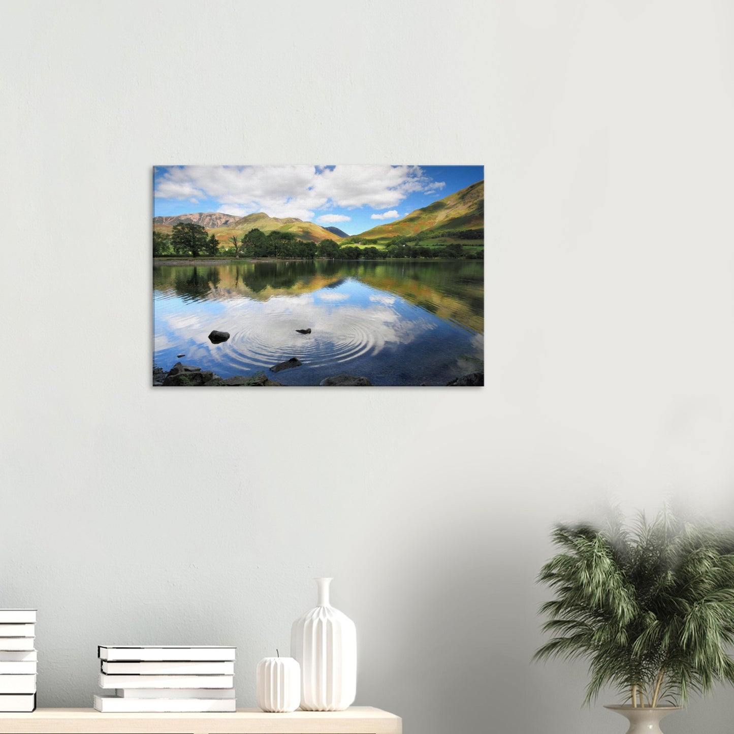 Reflective canvas print of Buttermere Lake with concentric ripples from a skipped stone and lush green hills under a cloud-patterned sky.