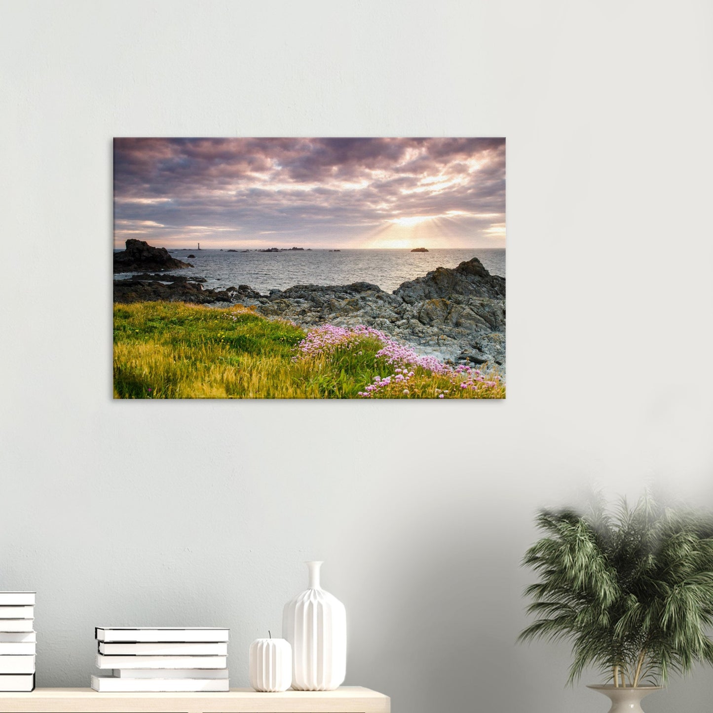 Canvas print of Pleinmont Point’s coastline at sunset with warm foreground lighting and Les Hanois Lighthouse on the horizon.