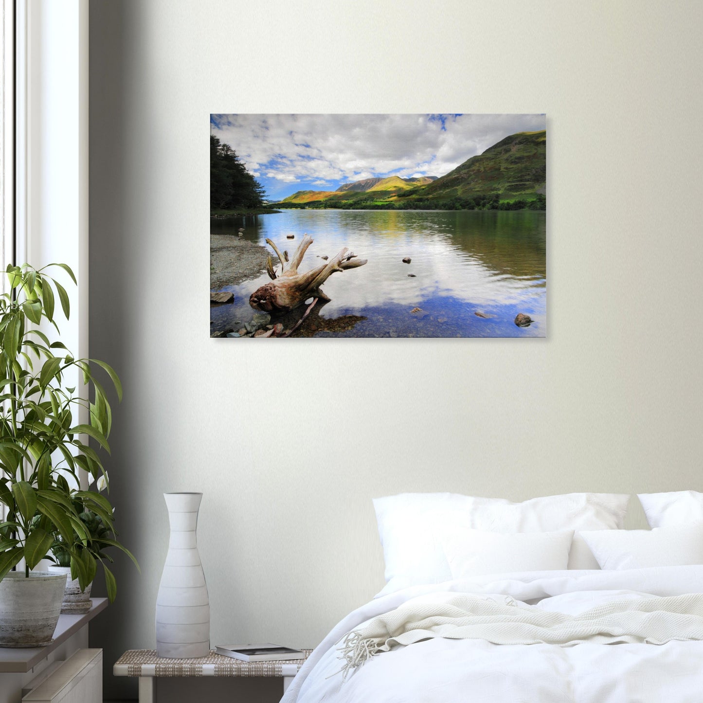 Canvas print capturing Buttermere Lake’s serene charm with calm reflective water, driftwood foreground, and sunlit green fells under a partly cloudy sky.
