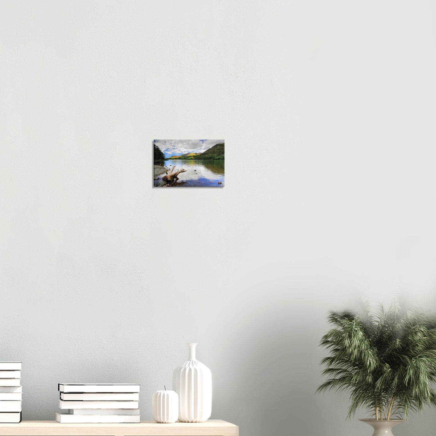 Canvas artwork of Buttermere Lake with calm water mirroring the sky and surrounding green fells, framed by a prominent piece of driftwood.