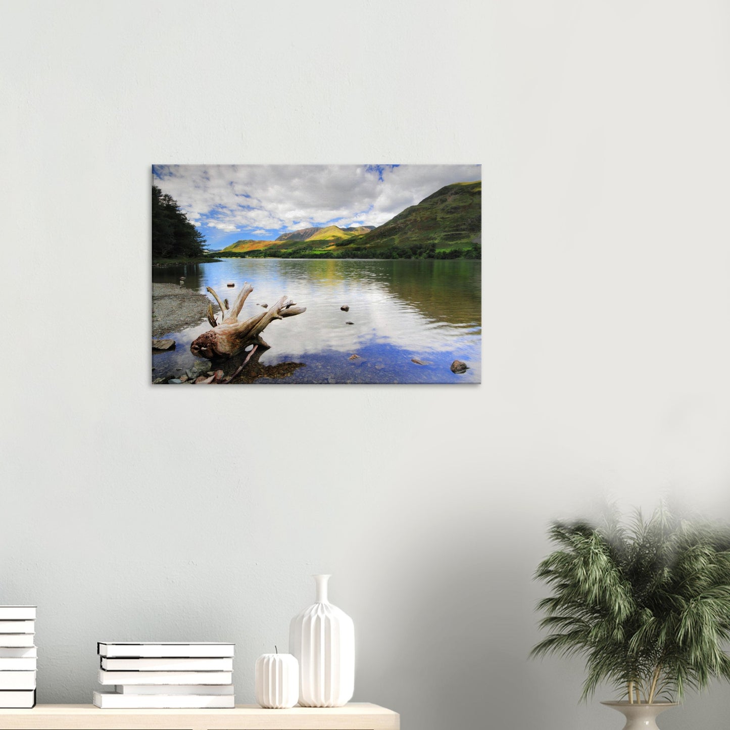 Peaceful Lake District canvas print of Buttermere Lake with calm water reflections, sculpted driftwood on the shore, and vibrant green hills.