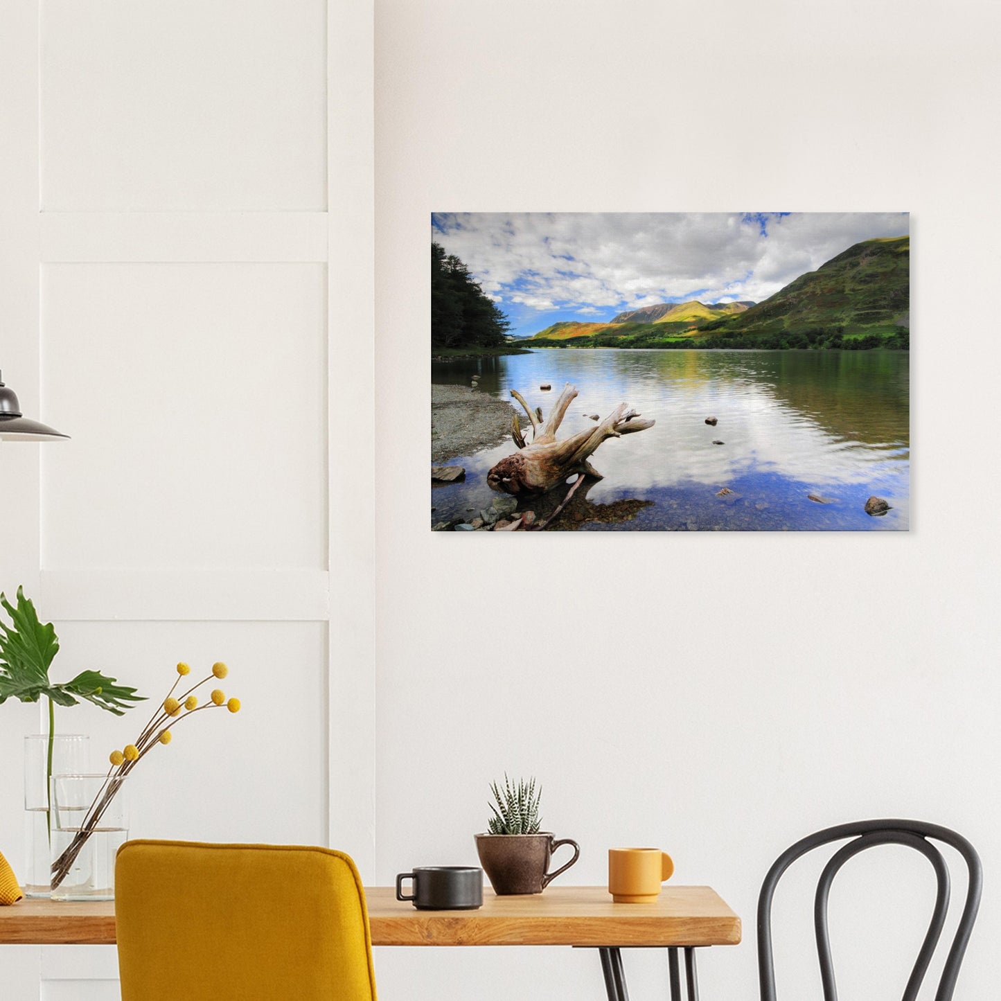 Buttermere Lake canvas print featuring reflective water, weathered driftwood in the foreground, and green hills illuminated by sunlight.