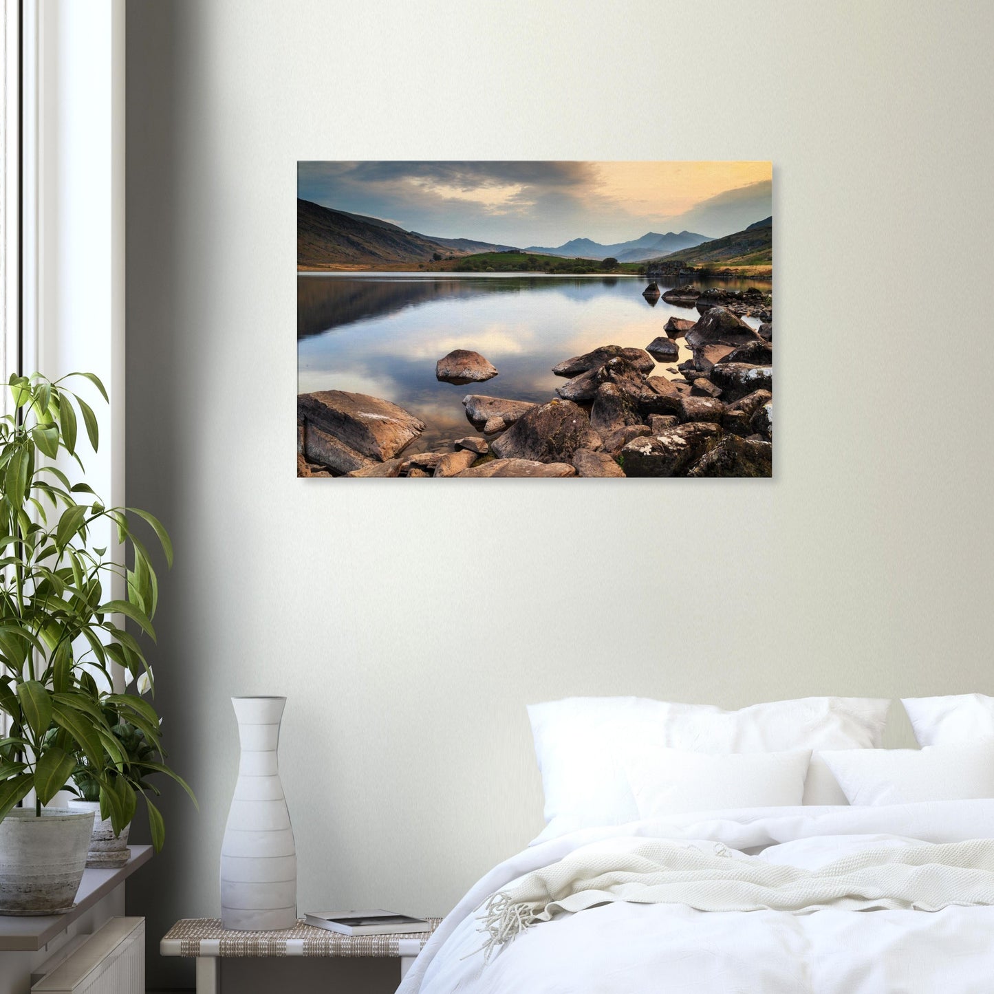 Softly lit sky and tranquil lake waters with foreground rocks guiding eyes toward Snowdonia peaks