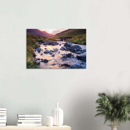 Scenic canvas featuring Honister Pass valley bathed in soft sunset hues, a gentle stream flowing under an old stone bridge.