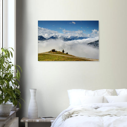 High-altitude canvas of Resterhöhe, Austria, showing dramatic contrast between green hilltop, cloud cover, and jagged snow-capped mountains.