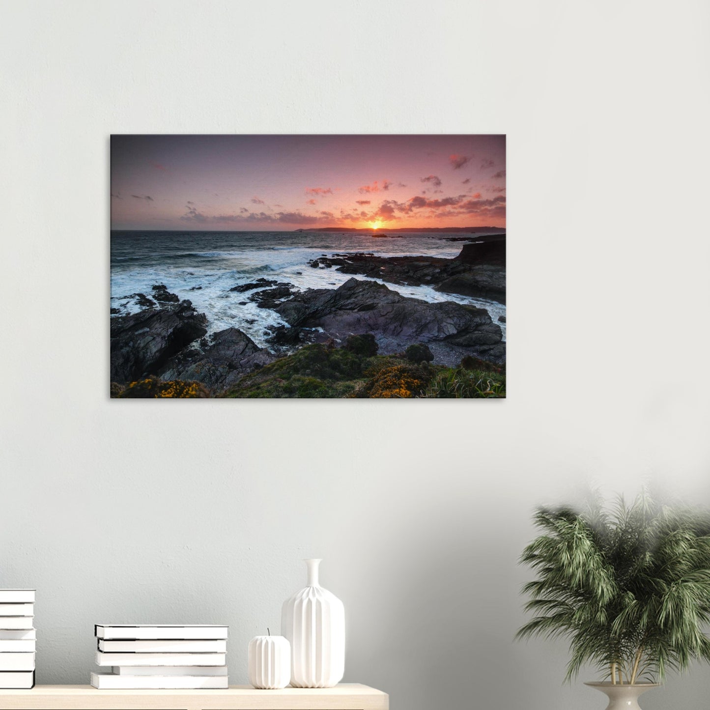 Canvas print of Heybrook Bay in Plymouth, Devon, showing a golden sunset illuminating rugged coastline, churning sea, and wildflowers on the cliffside.