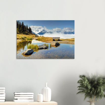 Austrian Alps canvas print with a reflective pond, peaceful bench, and dramatic mountain backdrop partially obscured by clouds.