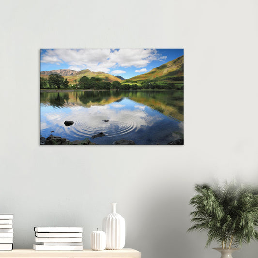 Canvas print of Buttermere Lake in the Lake District with gentle ripples disrupting the reflection of green fells and a cloud-dappled sky.