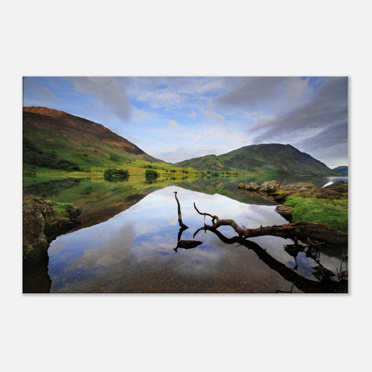 Reflective canvas print of Crummock Water with a natural branch in the foreground and mirror-like reflections of clouds and rolling fells.