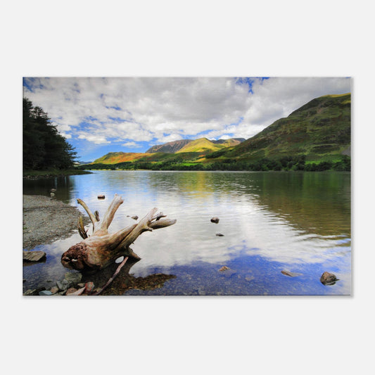 Tranquil landscape canvas print of Buttermere Lake with smooth reflective surface, sculpted driftwood, and vibrant green hills under a bright sky.
