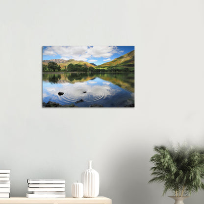 Reflective canvas print of Buttermere Lake with concentric ripples from a skipped stone and lush green hills under a cloud-patterned sky.