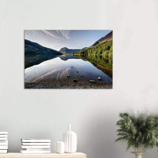 Canvas print of Buttermere Lake in the Lake District showing still waters reflecting surrounding fells and morning light on craggy peaks.
