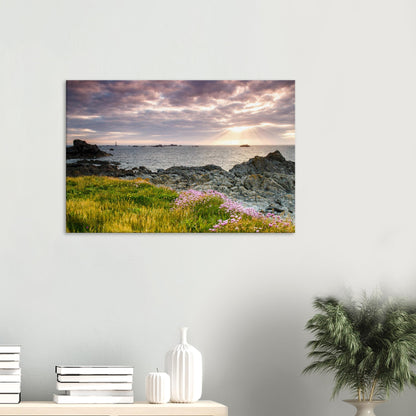 Canvas print of Pleinmont Point’s coastline at sunset with warm foreground lighting and Les Hanois Lighthouse on the horizon.