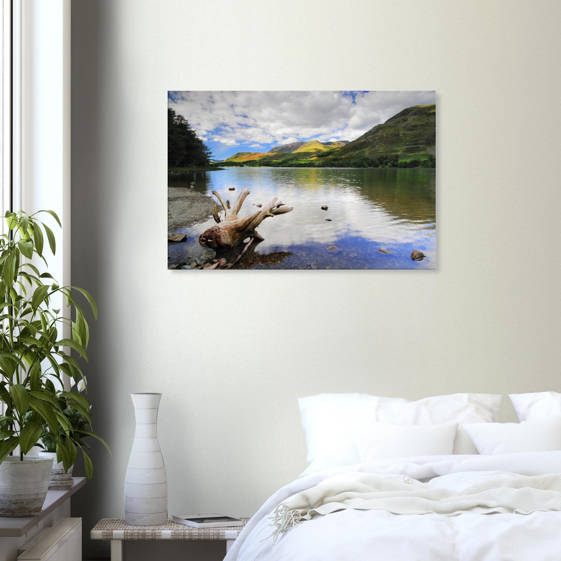 Canvas print capturing Buttermere Lake’s serene charm with calm reflective water, driftwood foreground, and sunlit green fells under a partly cloudy sky.