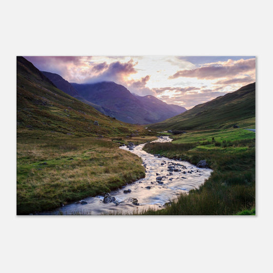 Canvas print of Honister Pass valley at golden hour, with sun-kissed hills, a winding brook, and misty mountains rising behind.