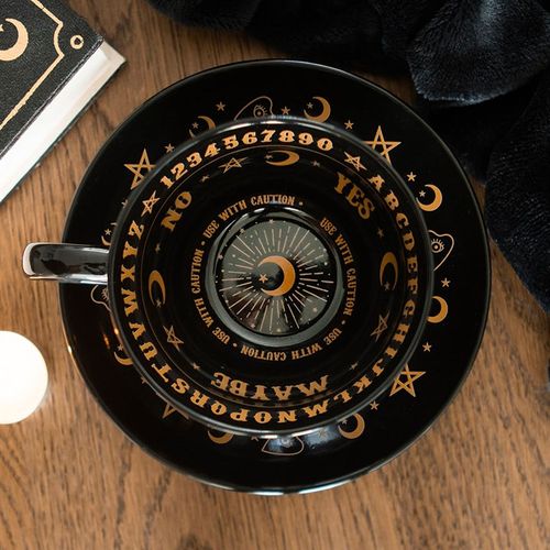 Ceramic teacup and saucer set with mystical talking board design in black and gold finish, perfect for tea leaf reading.