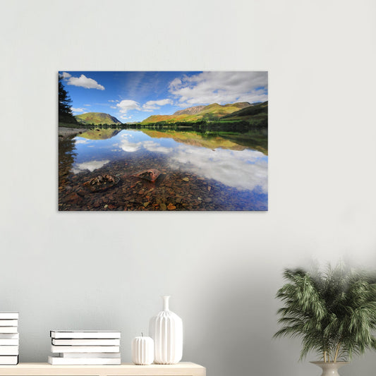 Canvas print of Buttermere Lake in the Lake District showing crystal-clear waters, a pebbled lakebed, and perfect reflections of green fells and fluffy clouds.