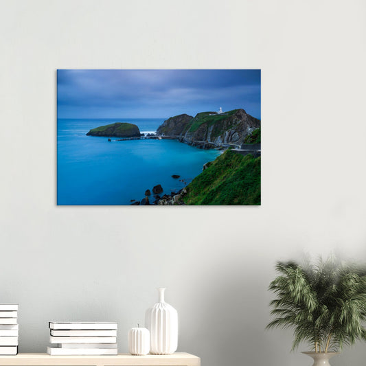 Canvas print of Landing Bay on Lundy Island at twilight, featuring a historic lighthouse atop rugged cliffs and calm blue waters.