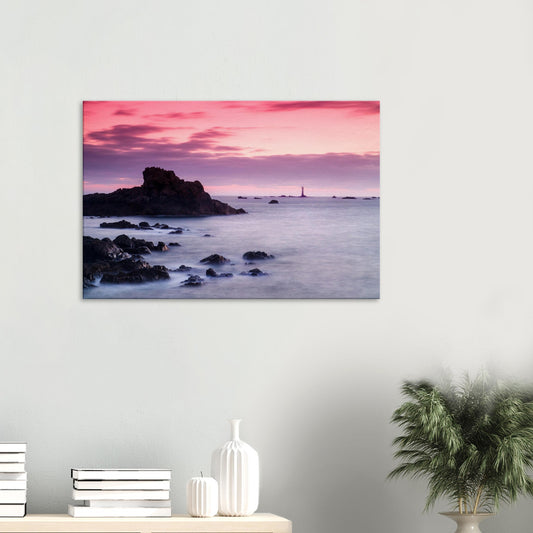 Canvas print of Les Hanois Lighthouse at sunset in Guernsey, silhouetted against a pink and purple sky above a calm sea.