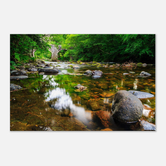 Serene river scene showing smooth stones and reflective waters beneath an ancient stone bridge