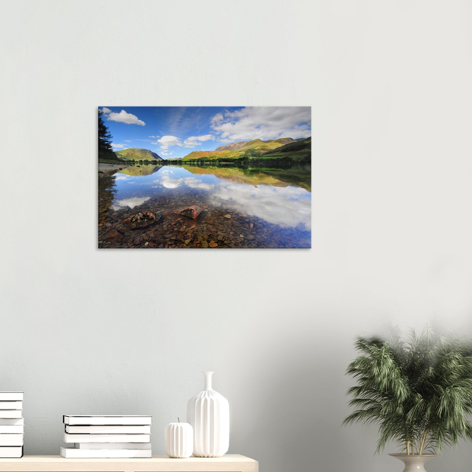 Canvas print of a peaceful moment at Buttermere Lake with glass-like water, visible stones beneath the surface, and crisp reflections of the surrounding fells.