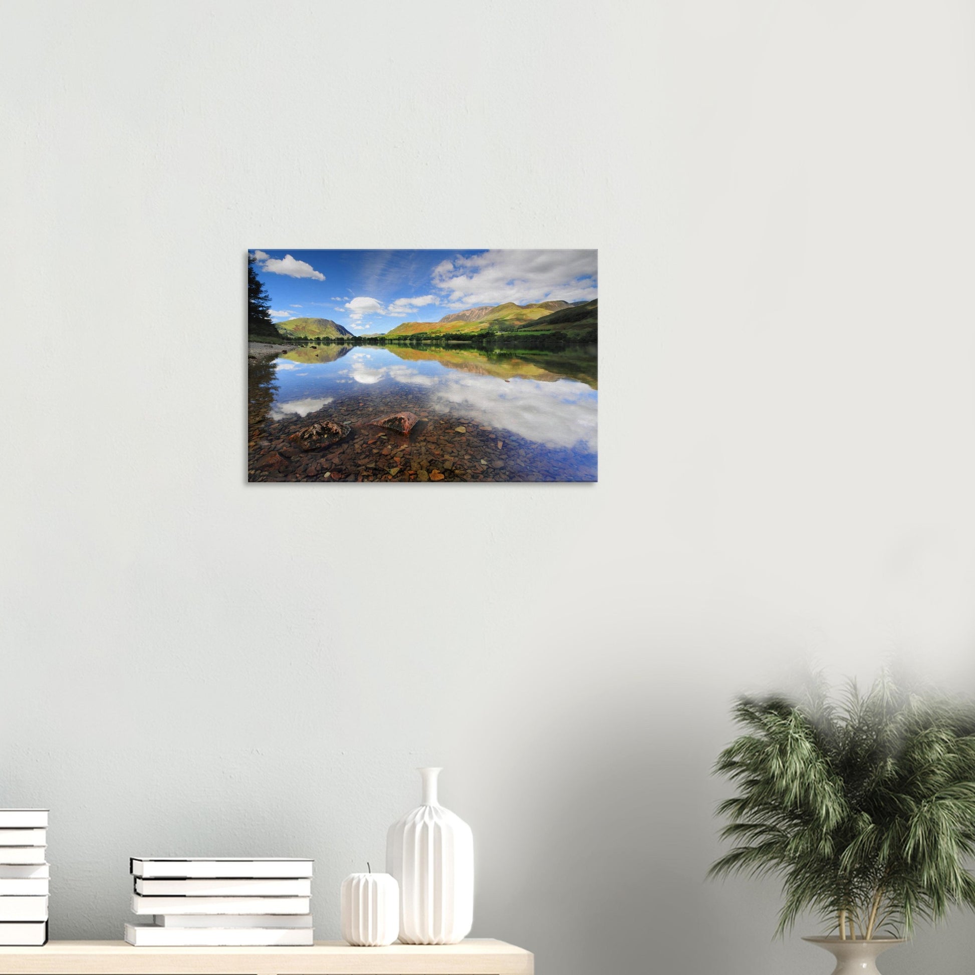 Peaceful canvas of Buttermere Lake with crystal-clear waters, visible pebbles, and mirrored reflections of green hills and a soft sky.