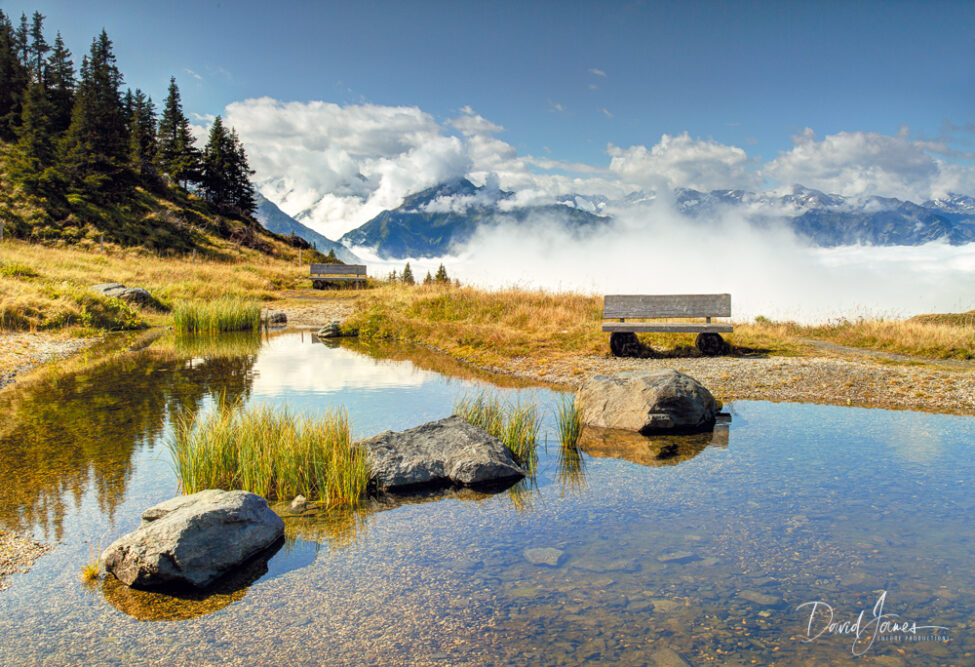 Fine Art Print of a reflective pond and bench at the Panoramabahn in Austria, with a backdrop of mountains and clouds